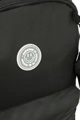 Mochila negra de tela con diseño liso, compartimento principal con cierre, bolsillo frontal con cierre y asa superior. Incluye un pequeño accesorio colgante de tela negra.