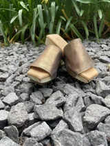 Zueco de mujer con plataforma de madera y suela de goma. La capellada es una tira ancha de cuero dorado metalizado, y la plantilla es acolchada.