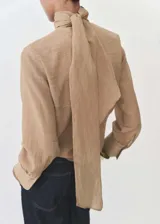 Blusa color beige con textura, cuello alto con lazo, mangas largas con puños abotonados y corte recto.