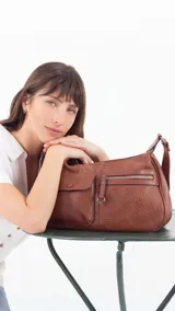 Bandolera color beige con correa ajustable, dos bolsillos frontales (uno con botón y otro con cierre) y un bolsillo trasero con cierre.