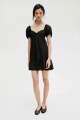 Vestido corto negro con escote corazón, mangas cortas abullonadas con elástico en hombros y puños, espalda fruncida y falda con vuelo.