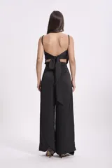 Pantalón de vestir color beige claro, tiro alto, de corte ancho y pierna recta. Presenta un detalle de tela drapeada o solapa larga que cae desde la cintura sobre la pierna izquierda.