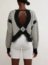 Buzo de tejido jacquard con patrón geométrico en tonos blanco roto y negro. Presenta cuello redondo, puños y bajo en rib negro, y un detalle de banda negra en las mangas.