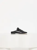 Mocasín tipo mule de cuero vacuno negro, con flecos y aplique metálico dorado en el empeine.
