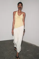 Vestido largo de fiesta con cuello halter fluido y hombros descubiertos. Presenta un top dorado drapeado y una falda larga color crema con textura.