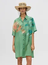 Camisa-vestido oversize de manga corta, color verde con estampado tie-dye en tonos salmón y turquesa. Presenta cuello camisero y cierre frontal de botones.