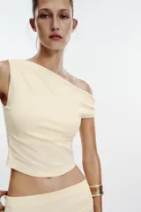 Top de color crema, con escote asimétrico y detalle de pliegues en el hombro.