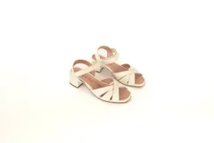 Sandalias de cuero color hueso, con tiras cruzadas en el empeine, talón descubierto y tobillera con hebilla. Taco cuadrado de 4 cm.