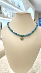 Collar corto con cuentas de cristal en verde y celeste, con dije de sol plateado con circonitas.