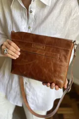 Cartera de mano tipo sobre, color beige claro, con solapa frontal decorada con una piedra de ágata azul engarzada en metal plateado. Posee correa larga ajustable de cuero beige.