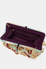 Bolso de mano tipo sobre con cuentas y abalorios multicolores. Tiene asa extraíble de cadena, bolsillo interior con cremallera y cierre con clip imantado y lazo.