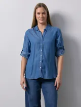 Camisa celeste de tencel con cuello con solapa, escote en V, abertura central con botones y mangas 3/4 regulables con presilla y botón.
