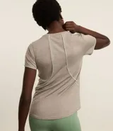 Remera deportiva de manga corta color beige melange, confeccionada en poliamida, con frisos blancos que recorren la espalda y los hombros.