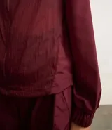 Campera deportiva rompevientos color bordó, con cuello alto, cierre frontal con cremallera, puños elastizados y recortes con hilo reflectante.