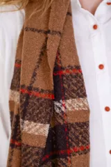 Bufanda rectangular grande con diseño escocés en tonos marrón, blanco, rojo y negro. Tiene flecos en los extremos.