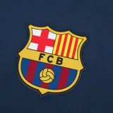 Short deportivo azul marino con cintura elástica y cordón ajustable. Presenta el escudo del FC Barcelona en la pierna derecha y la inscripción "Barça" en la pierna izquierda.