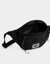Riñonera negra de tela deportiva con correa regulable, cierre superior con tirador de cordón y goma, bolsillo frontal con cierre y etiqueta de goma con texto "Brooklyn New York - NY Est. 1970".