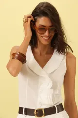 Camisa blanca sin mangas con cuello solapa y cierre frontal con botones.