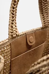 Bolso tipo shopper color marrón claro, con acabado trenzado. Tiene un compartimento principal con cierre de imán y un bolsillo plano interior. Cuenta con dos asas de mano.