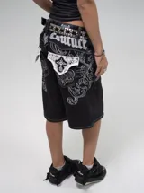 Bermuda de denim negro con bordados blancos estilo barroco/rococó en los bolsillos traseros y a lo largo de los costados. Presenta costuras contrastantes blancas, tiro medio y calce holgado (baggy fit). En la parte superior trasera lleva un aplique con el texto "Urban Coutur".