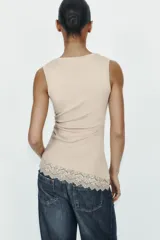 Camiseta ajustada (slim fit) de cuello redondo y manga sisa, color beige claro, con frunces laterales y bajo asimétrico con terminación de encaje a tono.