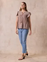 Blusa color marrón claro de algodón con bordados y calados blancos. Tiene cuello a la base, escote en V con lazo de ajuste y mangas cortas amplias.