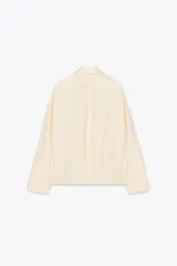 Cazadora tipo bomber color crema confeccionada en hilatura con mezcla de algodón. Cuello solapa y manga larga. Bolsillos delanteros. Forro interior a tono. Bajo ajustable. Cierre frontal con cremallera metálica.