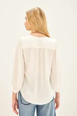 Camisa blanca de poliéster con cuello mao y mangas largas con frunces en hombros, mangas y espalda.