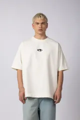 Remera color crema de corte oversize, con cuello redondo y mangas cortas. Presenta un pequeño bordado de un ojo en el frente.