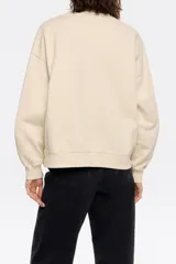 Sudadera color crema de algodón con cuello redondo y mangas largas. Estampado frontal con el logo de la marca y un dibujo de un perro.