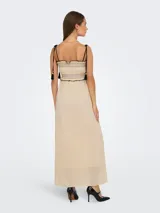 Vestido midi color crema, con tirantes finos ajustables, escote recto y cuerpo fruncido con detalle de borlas negras.