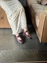 Zapatos de cuero color marrón con punta cuadrada, tira sobre el empeine con hebilla dorada y suela plana.