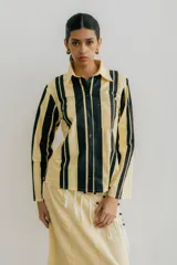 Camisa blanca con rayas verticales negras, de manga larga y corte recto. Tiene cuello clásico, cierre con botones y bolsillo en el pecho.