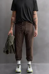 Pantalón de jogging color marrón oscuro, corte regular fit, confeccionado en tejido técnico ligero y elástico. Cuenta con cintura elástica ajustable con cordón, bolsillos frontales con cierre de cremallera, bolsillo trasero con cierre de cremallera oculta en costura y bajo ajustable con elástico.