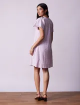 Vestido corto de lino a rayas verticales color lila y blanco, con cuello fruncido, escote en V y lazo de ajuste. Mangas cortas con puntilla de crochet.