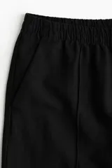 Pantalón negro de lino con cintura elástica, bolsillos laterales y traseros. Piernas rectas con pliegue cosido adelante.