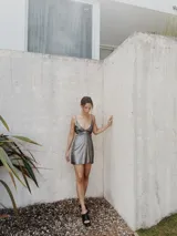 Vestido corto plateado metalizado con escote en V profundo, breteles finos, aberturas en la cintura y espalda descubierta.