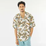 Camisa de manga corta blanca con estampado de hojas en tonos marrones, verdes y amarillos. Tiene cuello clásico, cierre frontal con botones y corte recto.