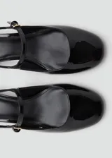 Zapato destalonado negro de efecto charol, con tacón bloque bajo y puntera redondeada. Presenta una tira fina con hebilla ajustable sobre el empeine.