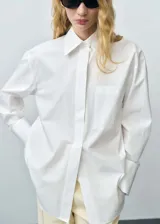 Camisa blanca oversize de algodón orgánico, con cuello camisero, manga larga con puños abotonados, bolsillo de parche en el pecho y cierre frontal con botones.