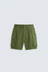 Bermuda color verde militar, relaxed fit, confeccionada en tejido técnico ligero. Cintura elástica ajustable con cordón interior, pliegues frontales, bolsillos delanteros y traseros con solapa, bolsillos cargo con solapa en perneras. Cierre frontal con cremallera y botón.