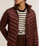 Campera puffer ultraligera color marrón, confeccionada en poliamida acolchada, con cuello alto y cierre por cremallera. Incluye bolsita con cordón.