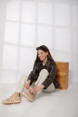 Chaqueta de cuero ovino color marrón oscuro, con cuello camisero, cierre frontal de botones y bolsillos verticales con cierre en la parte delantera. Presenta un corte recto y holgado.