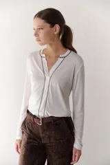 Remera blanca de mangas largas con escote en V y costuras decorativas en negro.