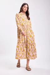 Vestido midi de corte holgado con estampado floral en tonos rosa y amarillo. Tiene cuello camisero, mangas largas con puños elásticos y falda escalonada.