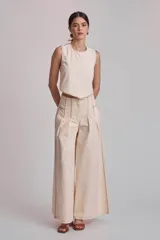 Pantalón ancho de tiro alto color crema, con pinzas frontales y pespuntes contrastantes en color marrón oscuro a lo largo de los paneles y costuras.