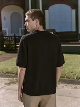 Polo negro de manga corta con cuello clásico y cierre de dos botones. Tejido de punto plano con textura ligera y fit relajado.