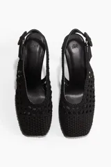Zapatos de tacón destalonados color negro, confeccionados en lona de algodón con diseño trenzado. Modelo con punta cuadrada y tira ajustable en el talón con hebilla redonda revestida.