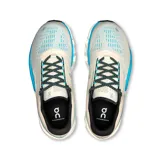 Championes de running On Running Cloudmonster 2, color crema con detalles en turquesa y verde. Presentan el logo de la marca en el lateral y suela con tecnología CloudTec.
