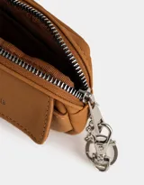 Monedero color marrón camel de suede con bolsillo frontal con solapa y broche con botón para cerrado. Tiene cierre superior con mosquetón y tag en relieve con la inscripción "Girls Club".